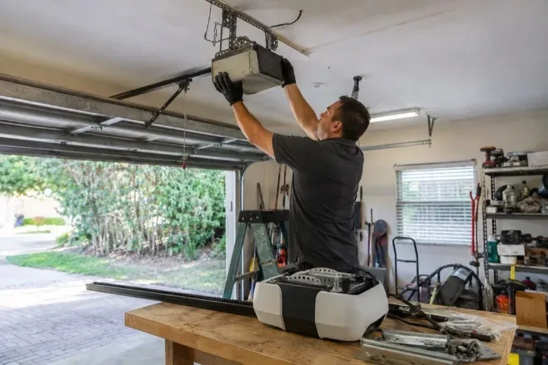 Person holding an overhead garage-door opener beside another opener and hardware on a workbench — Garage Door Opener Replacement, Burlington