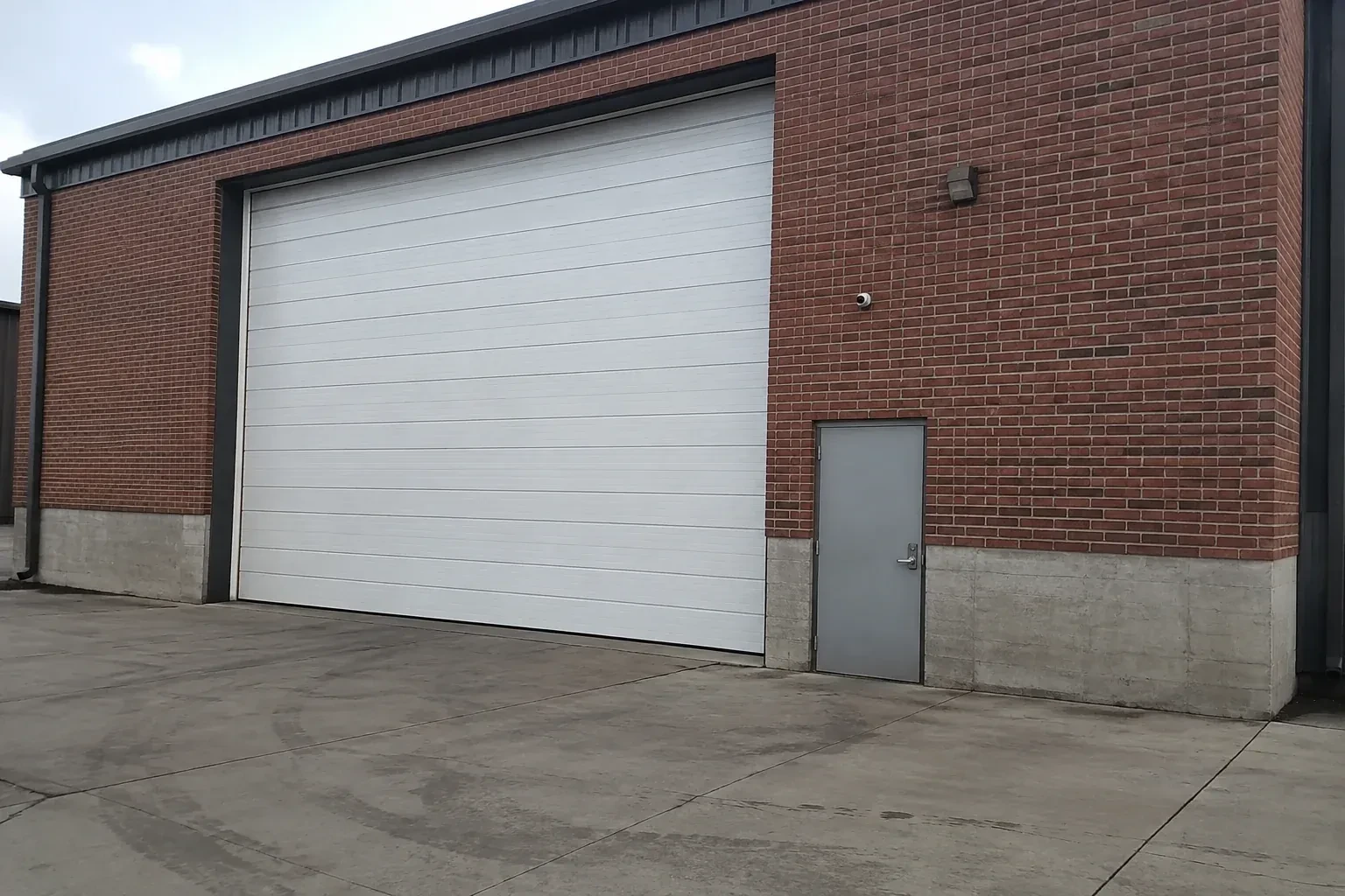 Tall closed sectional loading door beside a personnel door at a brick unit. — Commercial Sectional Door Repair, Burlington